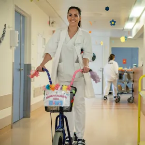 En person i hvit frakk som skyver en barnevogn med en kurv med blomster