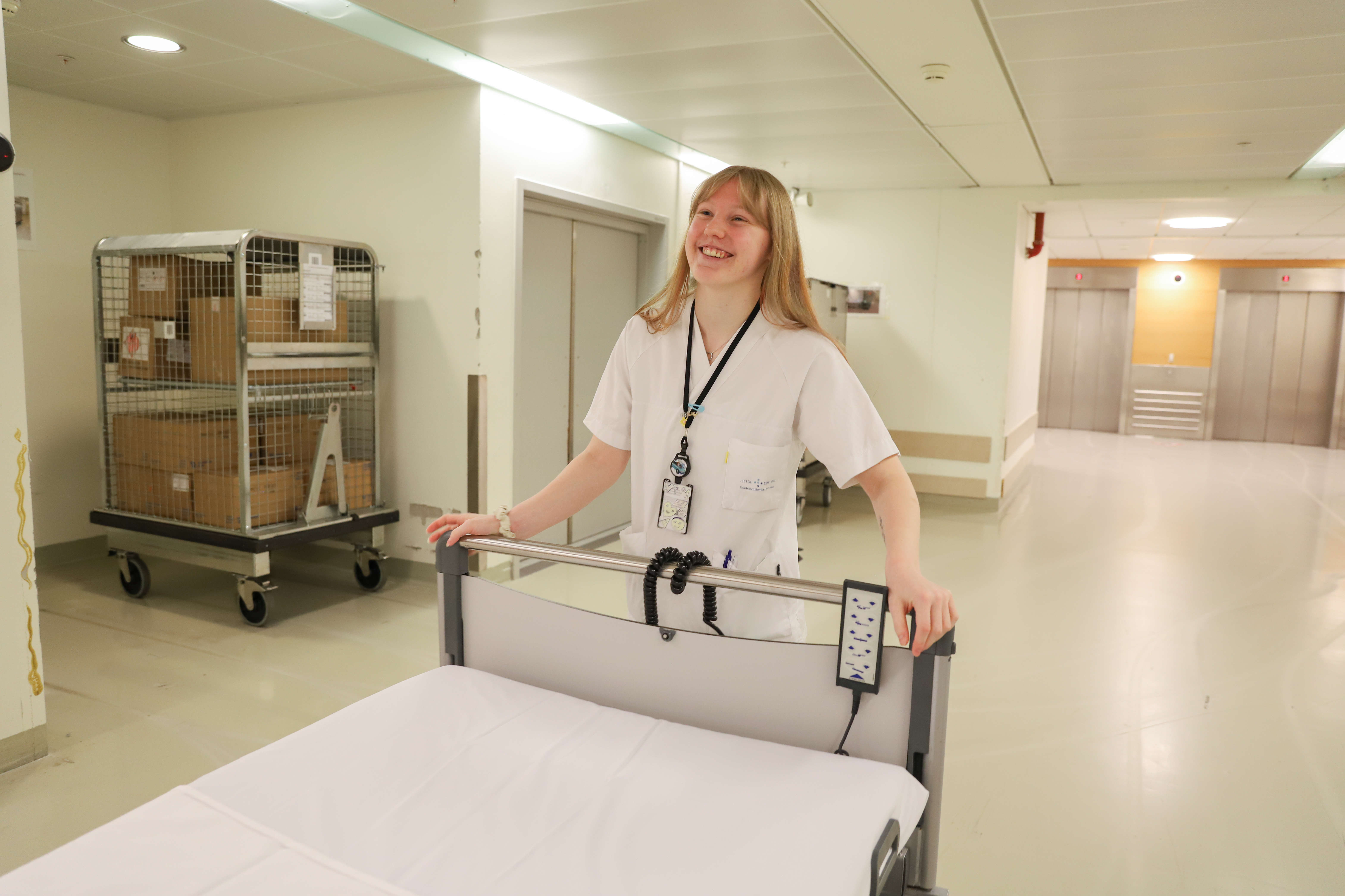 en kvinne i hvit sykehusuniform smiler mot kamera