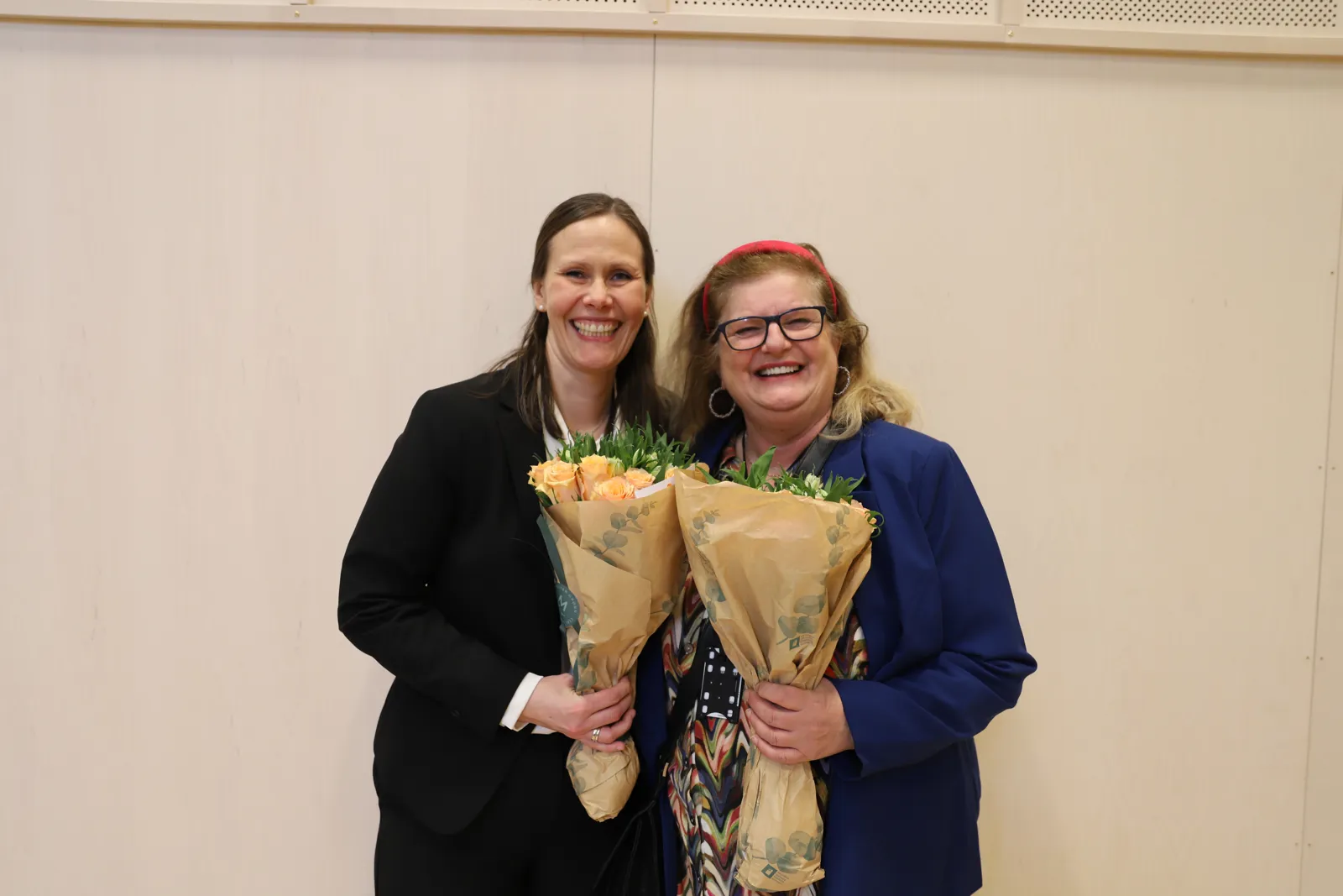 To kvinner med blomster smiler mot kamera