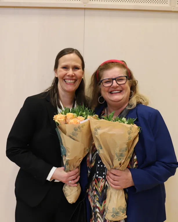 To kvinner med blomster smiler mot kamera