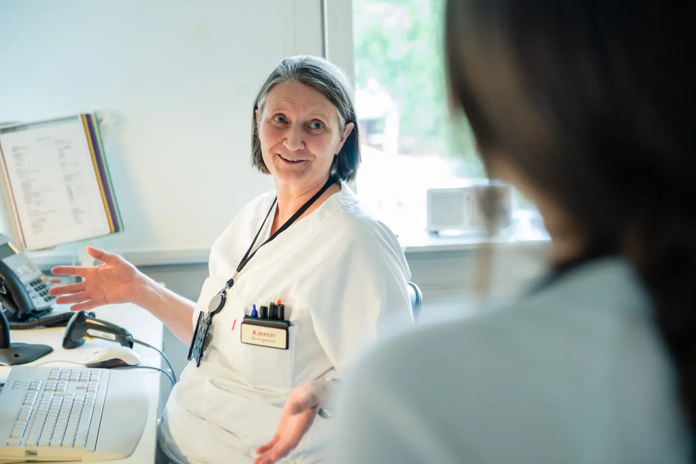 Kvinne foran data snakker med et annet menneske som har ryggen mot kamera