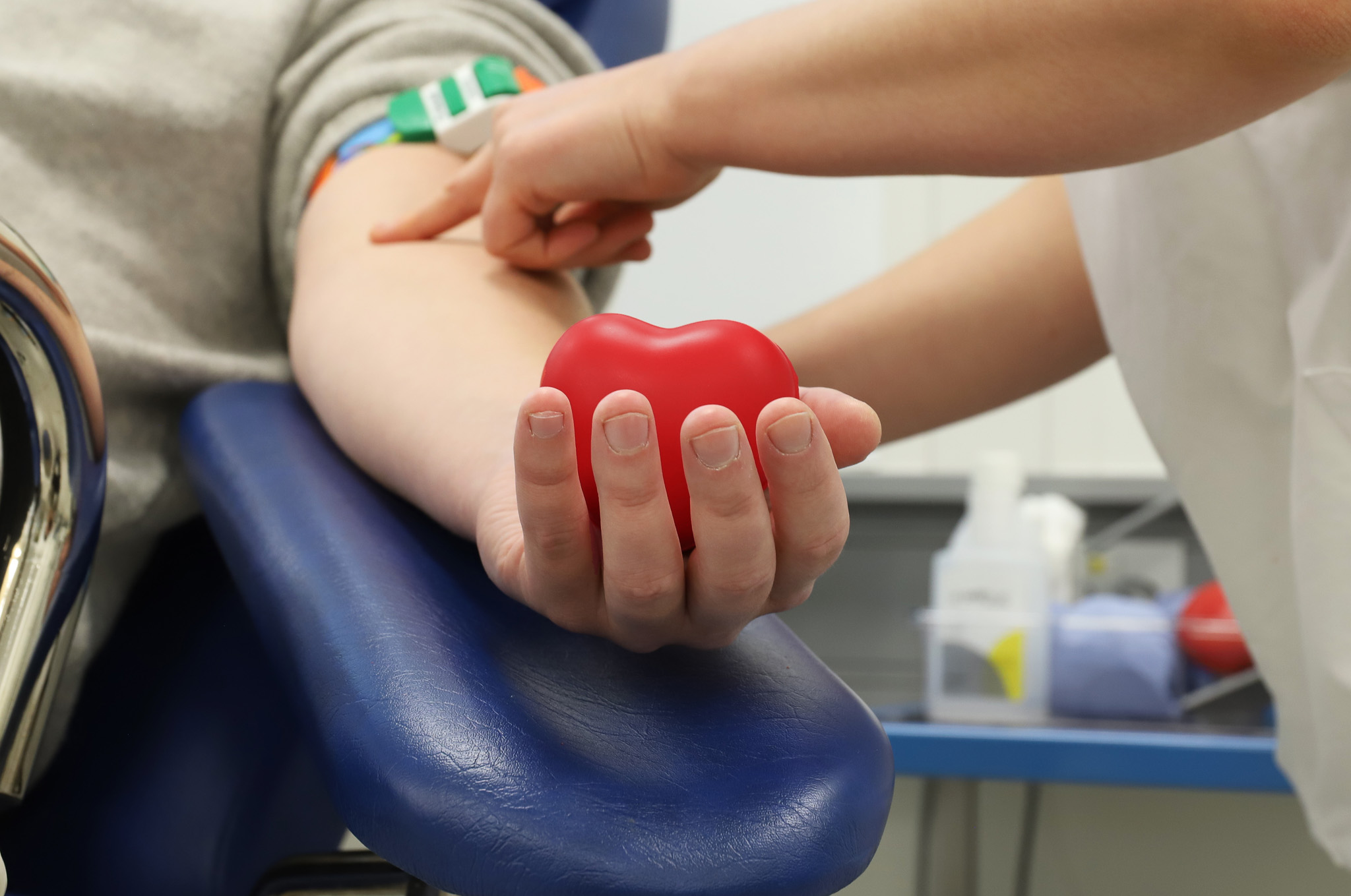 Bildet viser en blodgiver som holder en gummiball formet som et hjerte, mens sykepleieren leter etter en blodåre.