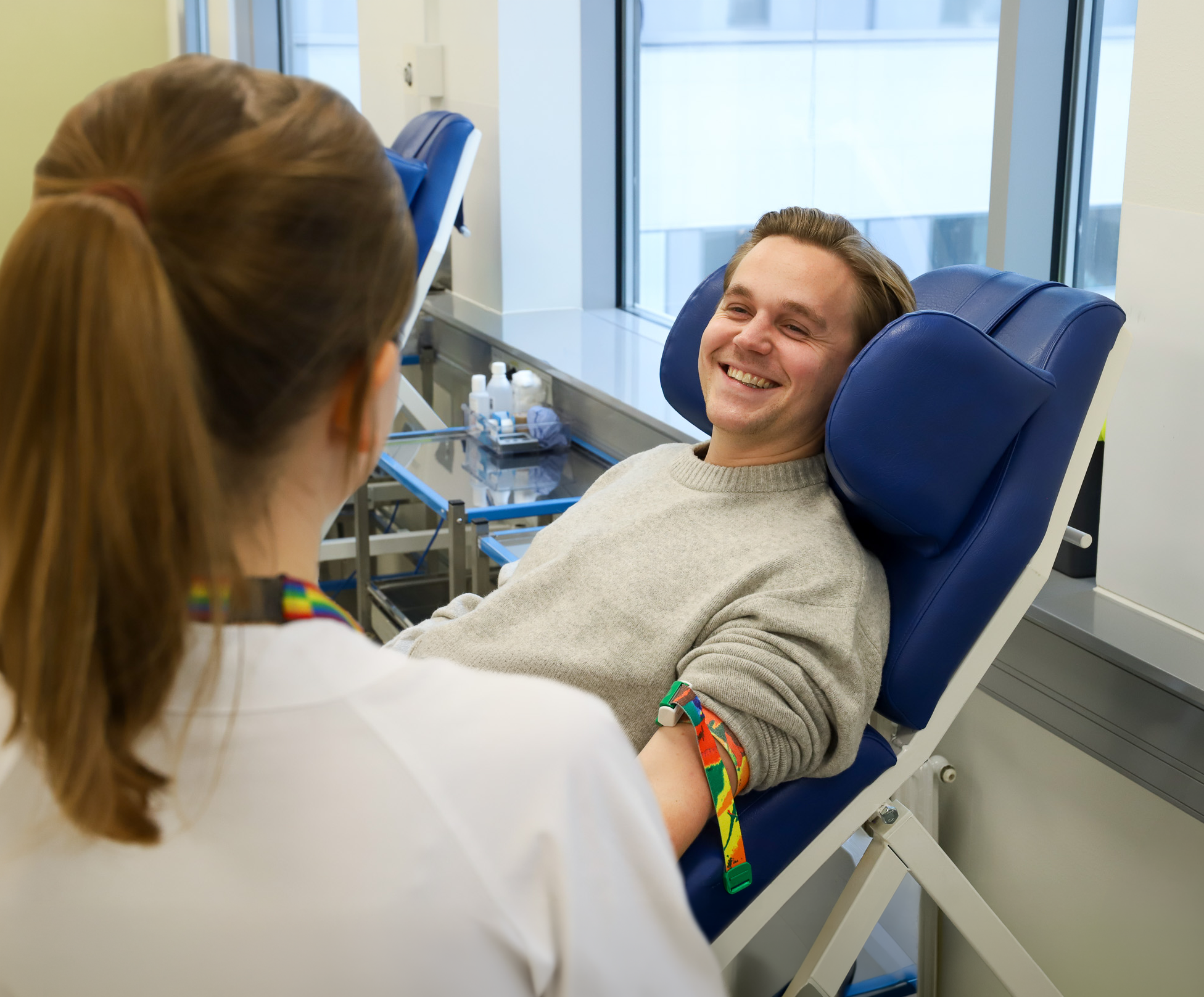 Blodgiver sitter i en behandlingsstol og smiler til sykepleieren.