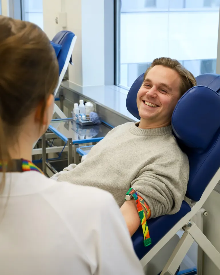 Blodgiver sitter i en behandlingsstol og smiler til sykepleieren.