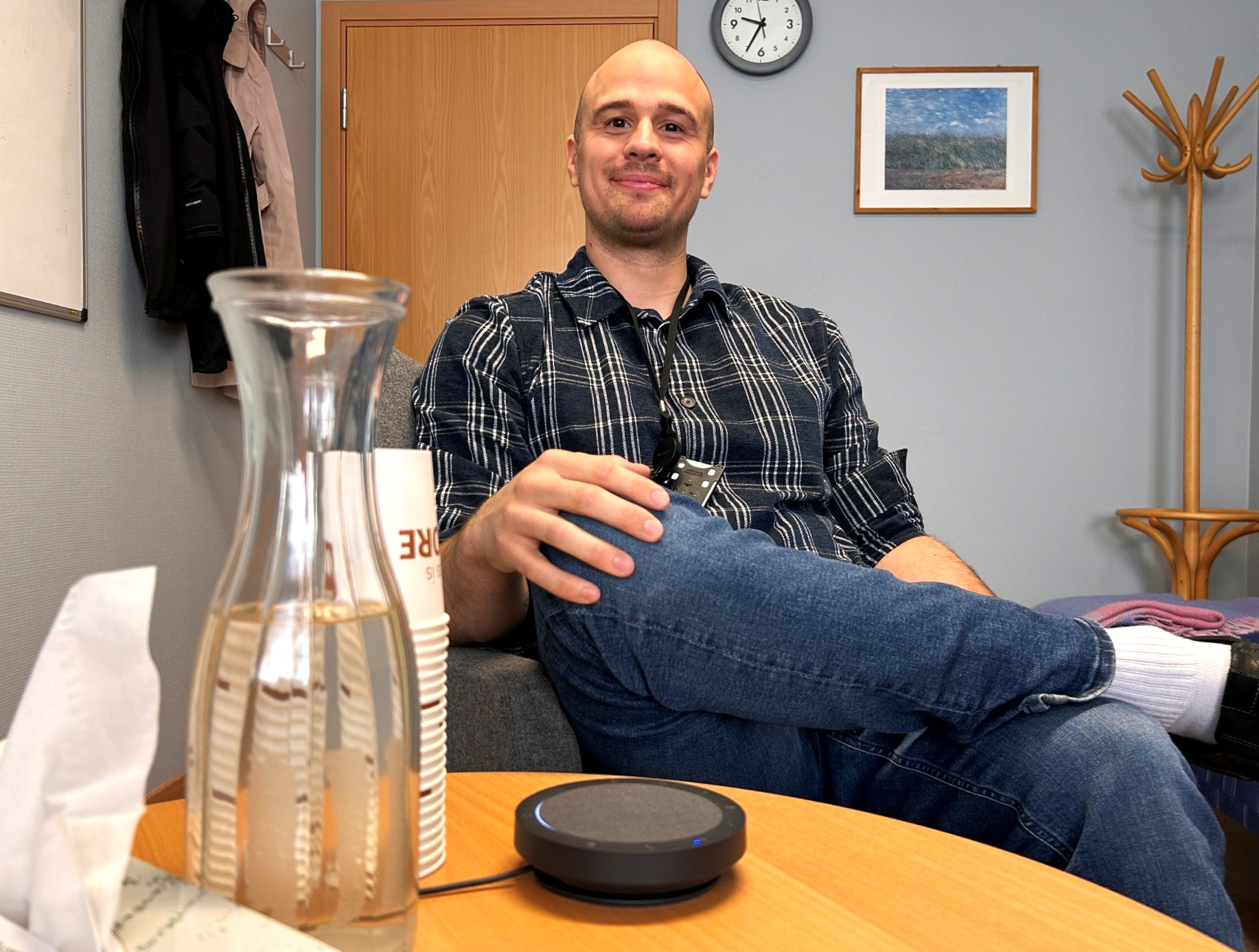 Avslappet mann venter bak et bord med vannkaraffel, papir og opptaksutstyr