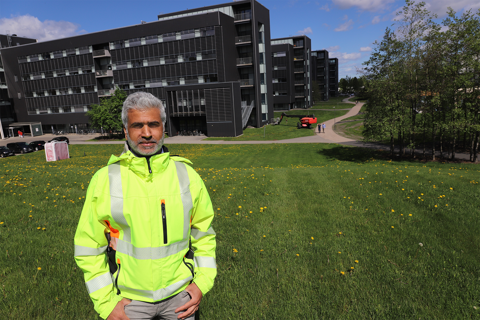 En mann med sikkerhetsvest står på en gresseng med en bygning i bakgrunnen