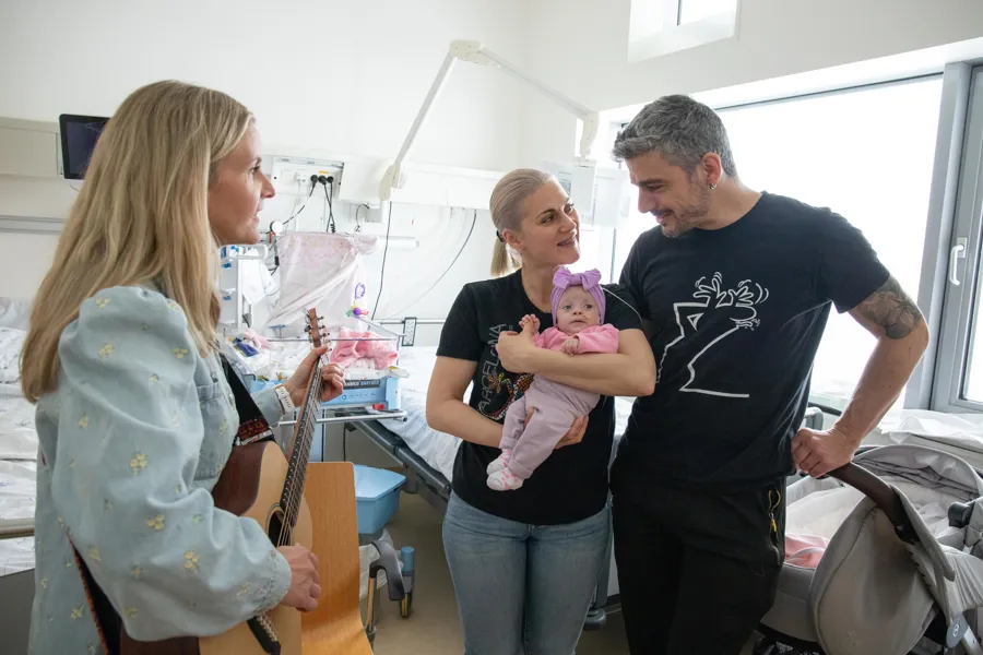En mann og kvinne som holder en baby foran en dame som spiller gitar
