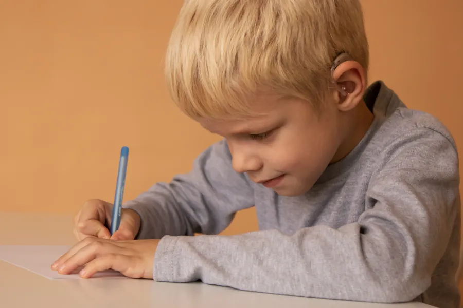 En gutt med høreapparat skriver på et ark
