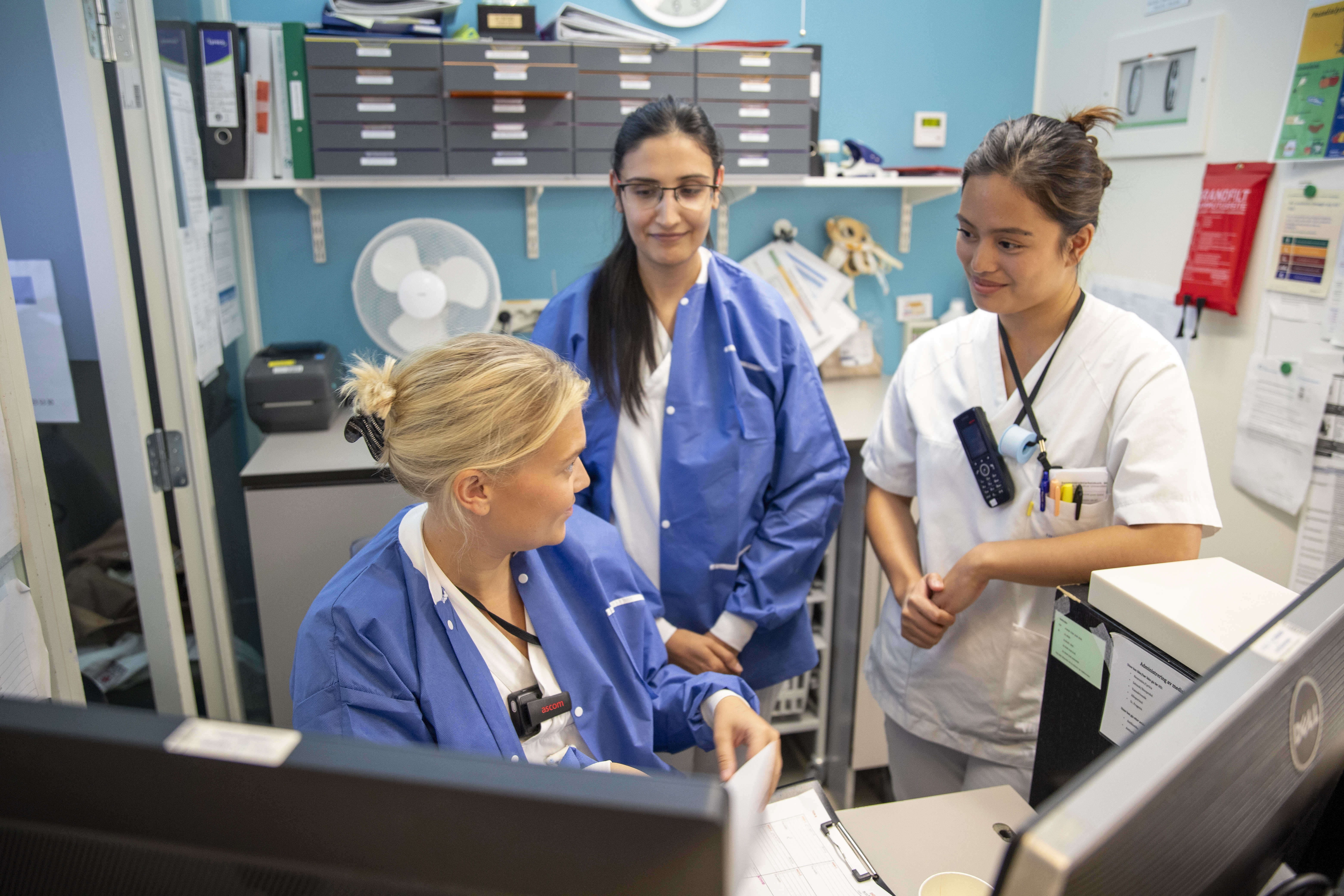 tre sykepleiere snakker sammen på en sengepost
