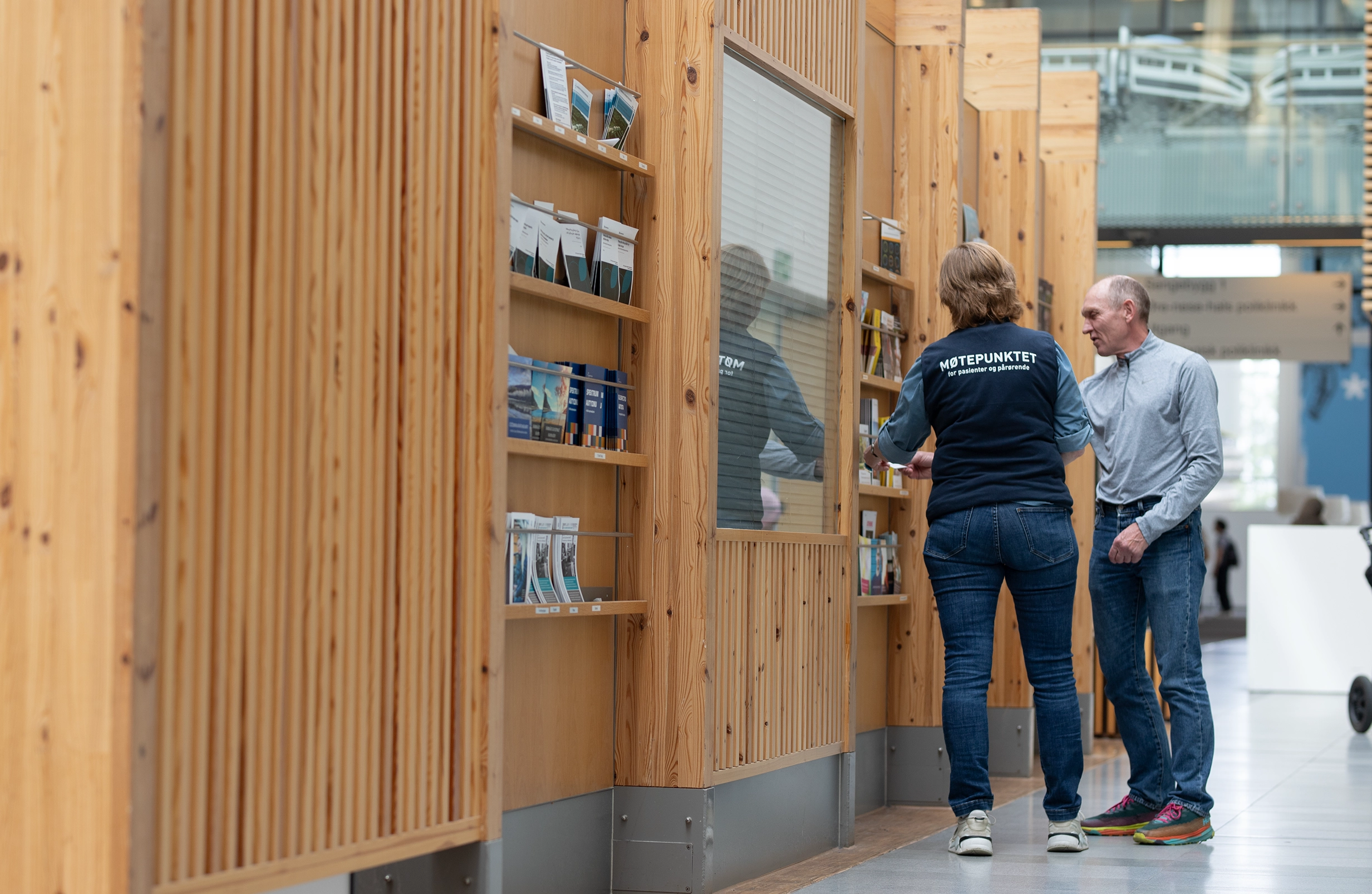 To personer står ved en bokhylle som er full av brosjyrer og blader