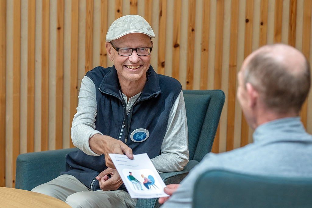 En person som smiler og gir en brosjyre til en annen person