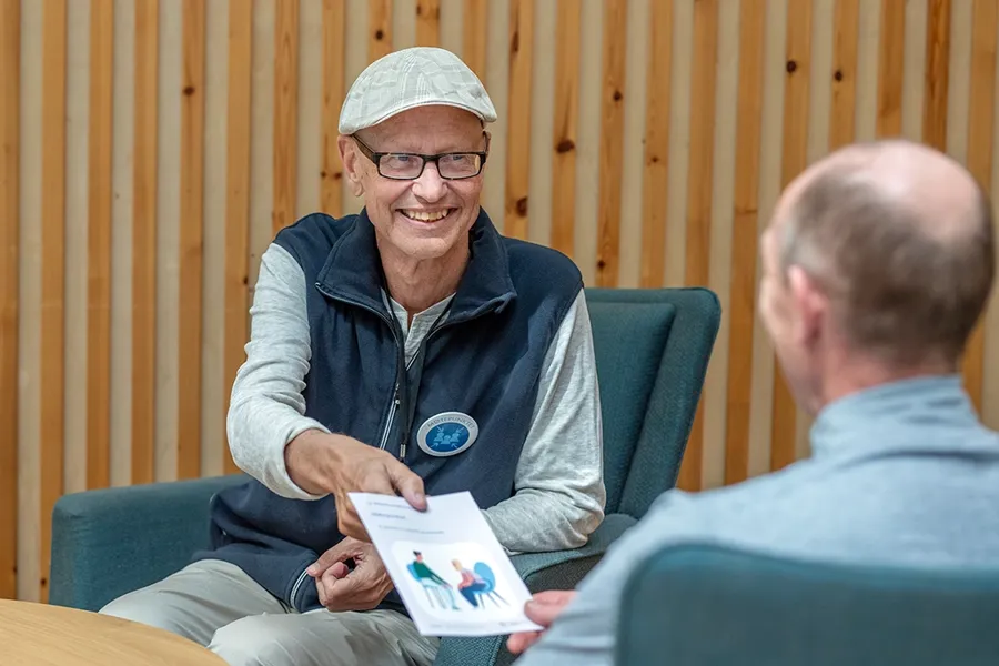 En person som smiler og gir en brosjyre til en annen person