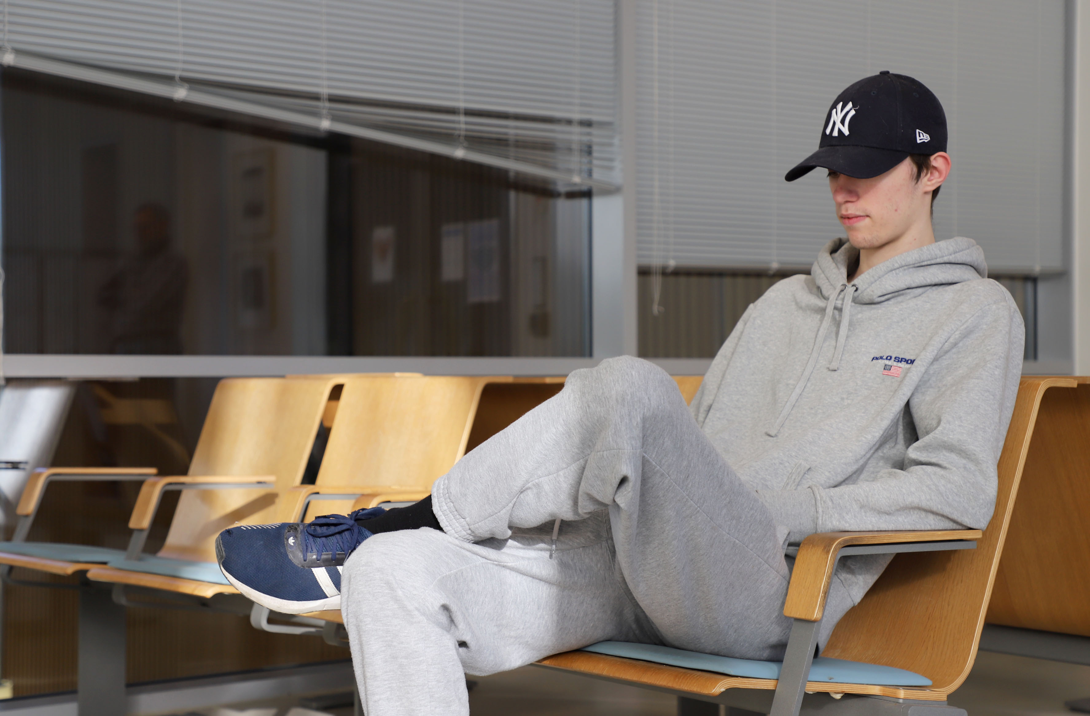 Gutt med caps sitter på venterom og ser på mobilen