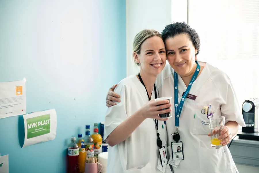 To kvinnelige sykepleiere holder rundt hverandre og smiler.