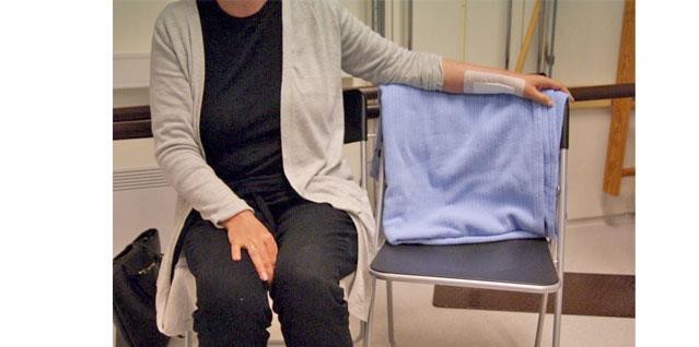 Kvinne sitter i stol med en arm over ryggstøtten på en stol som står ved siden av seg