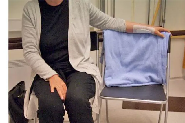 Kvinne sitter i stol med en arm over ryggstøtten på en stol som står ved siden av seg