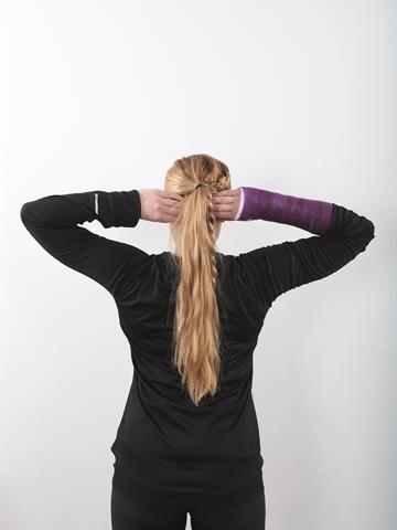 Kvinne står med ryggen til og armen opp, med hendene hvilende på bakhodet