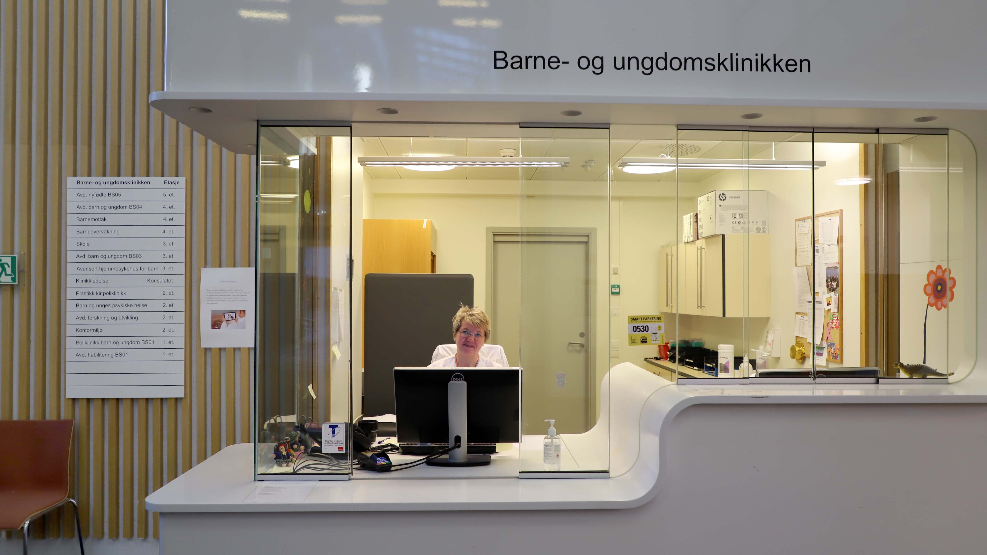 Resepsjonisten på Barne- og ungdomsklinikken smiler bak respesjonen 