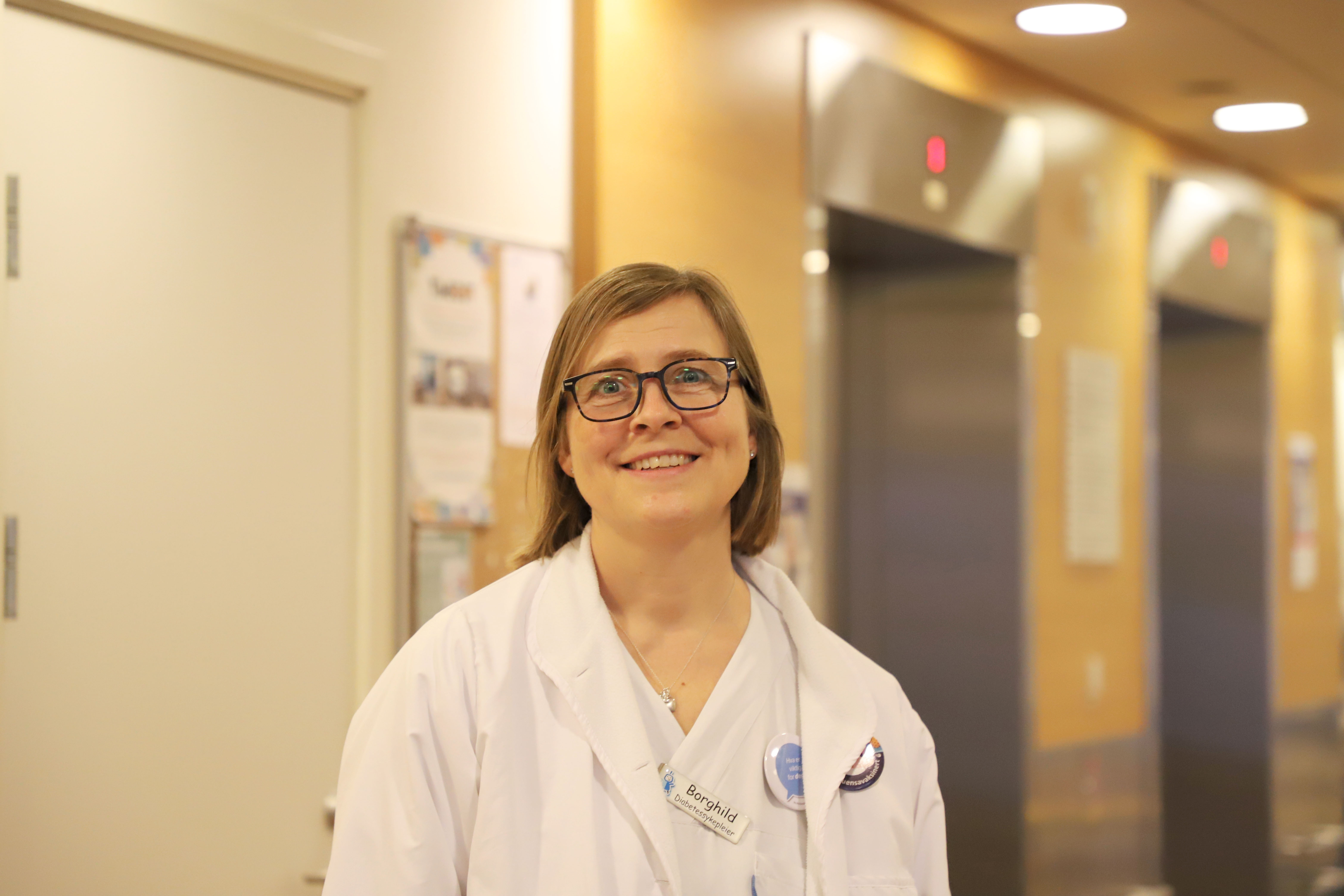 En kvinne med brunt hår og firkantede briller smiler til kamera