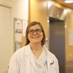 En kvinne med brunt hår og firkantede briller smiler til kamera