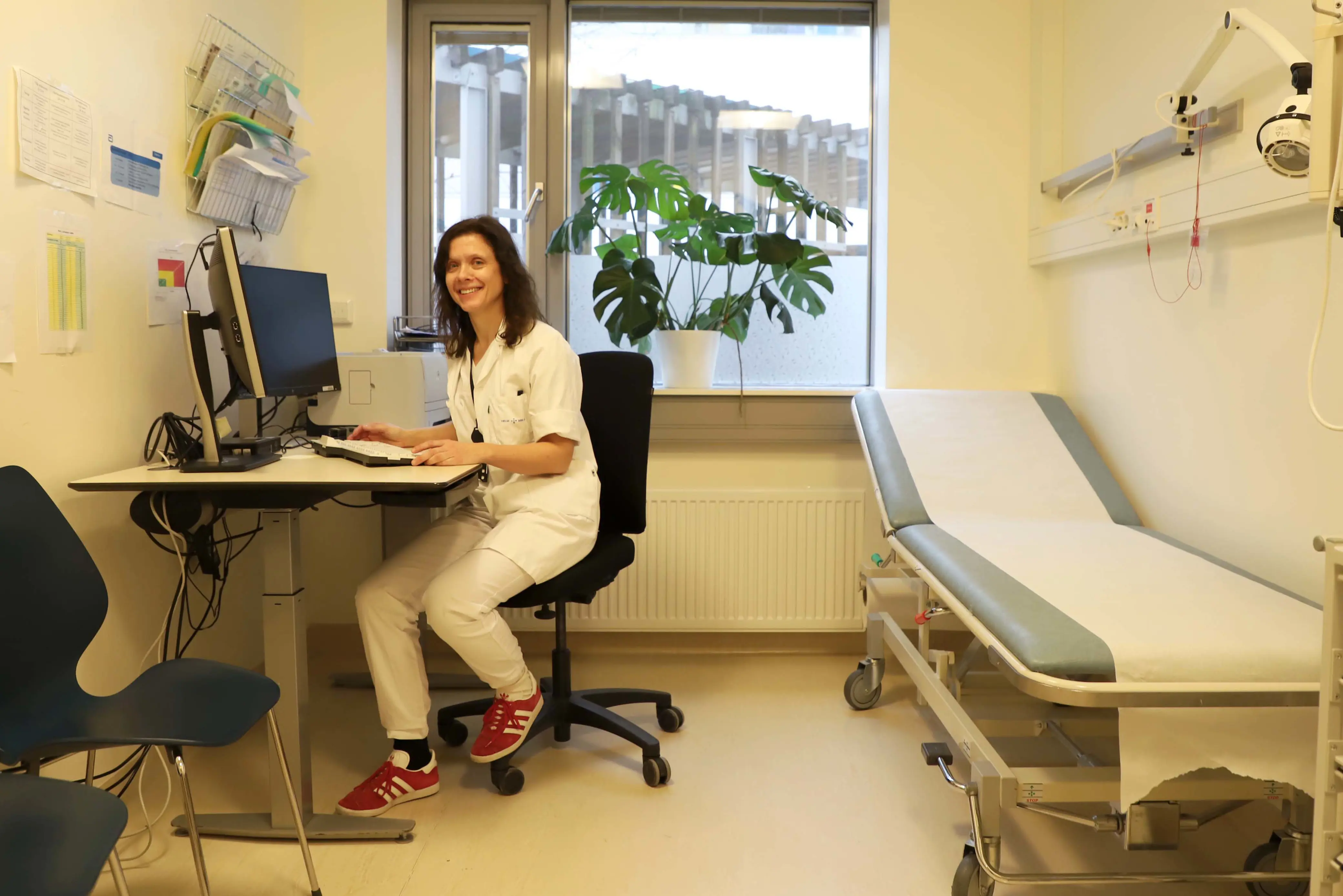 En blid kvinne sitter på kontorstol inne på et legekontor