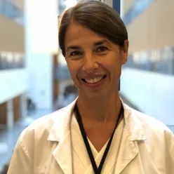 En kvinne med brunt hår i hestehale og hvit legefrakk smiler