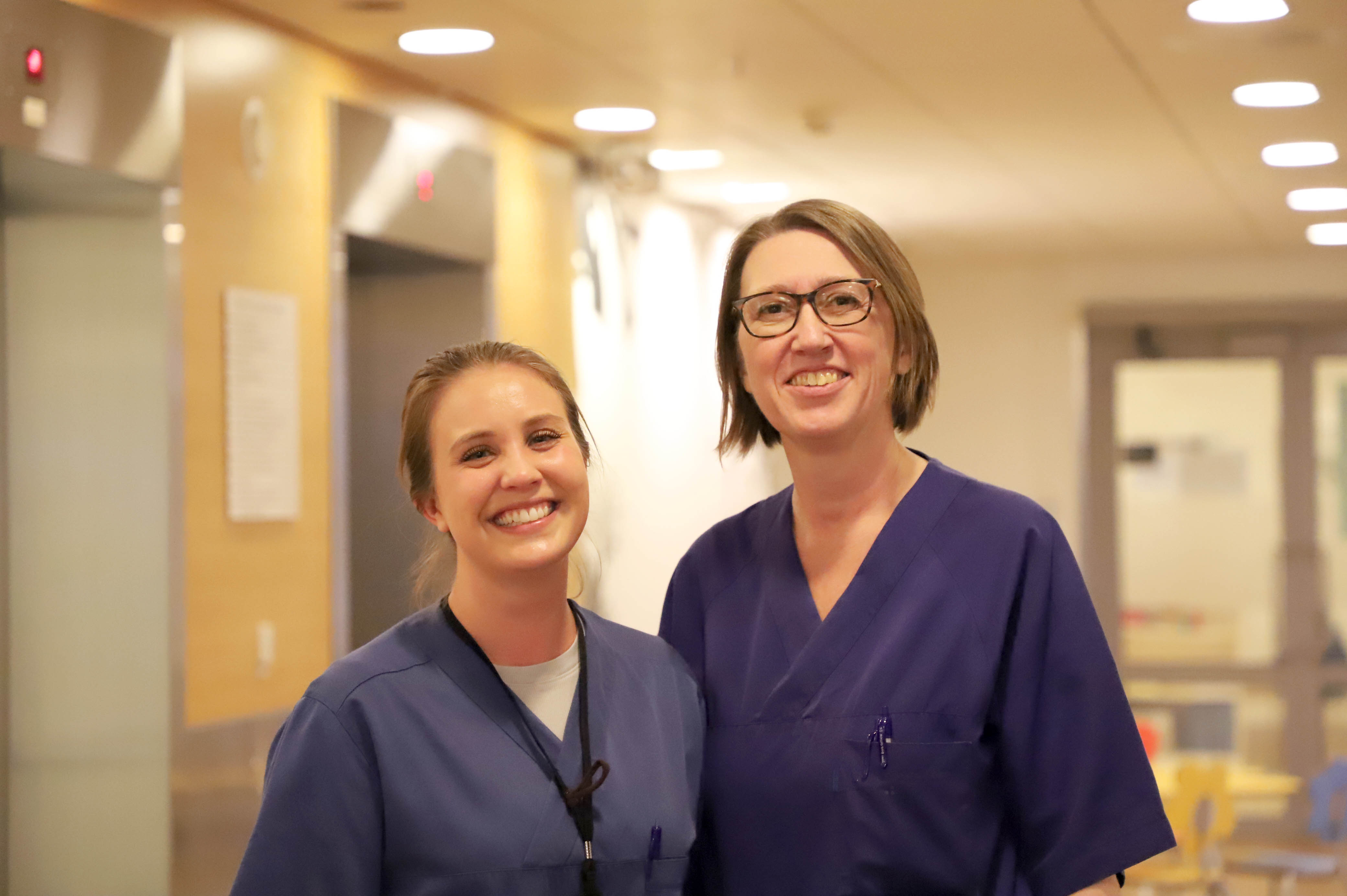 To kvinner med mørkt hår og lilla t-skjorter smiler bredt