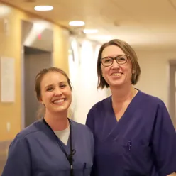 To kvinner med mørkt hår og lilla t-skjorter smiler bredt