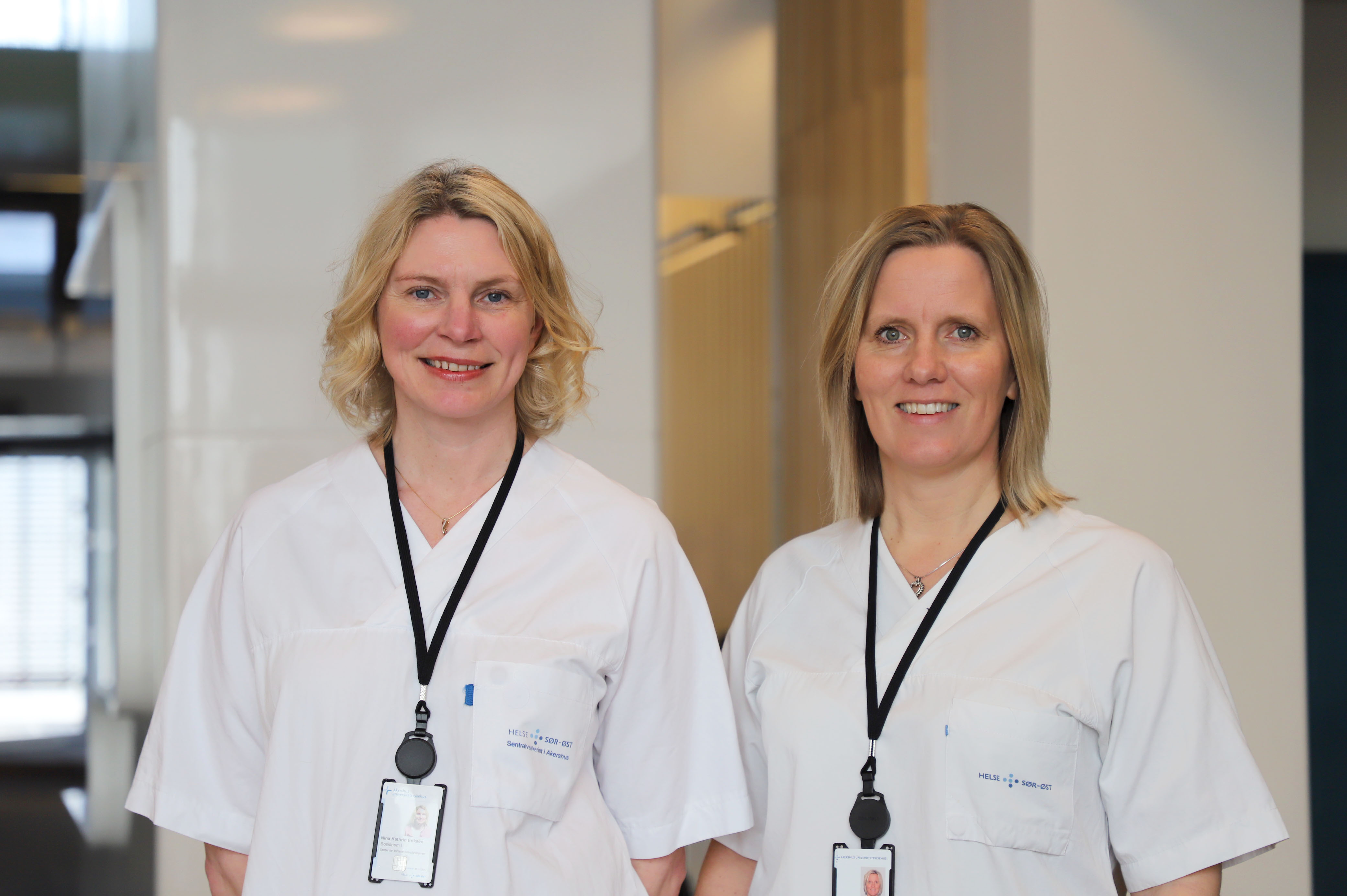 To kvinner med blondt hår og hvite frakker smiler