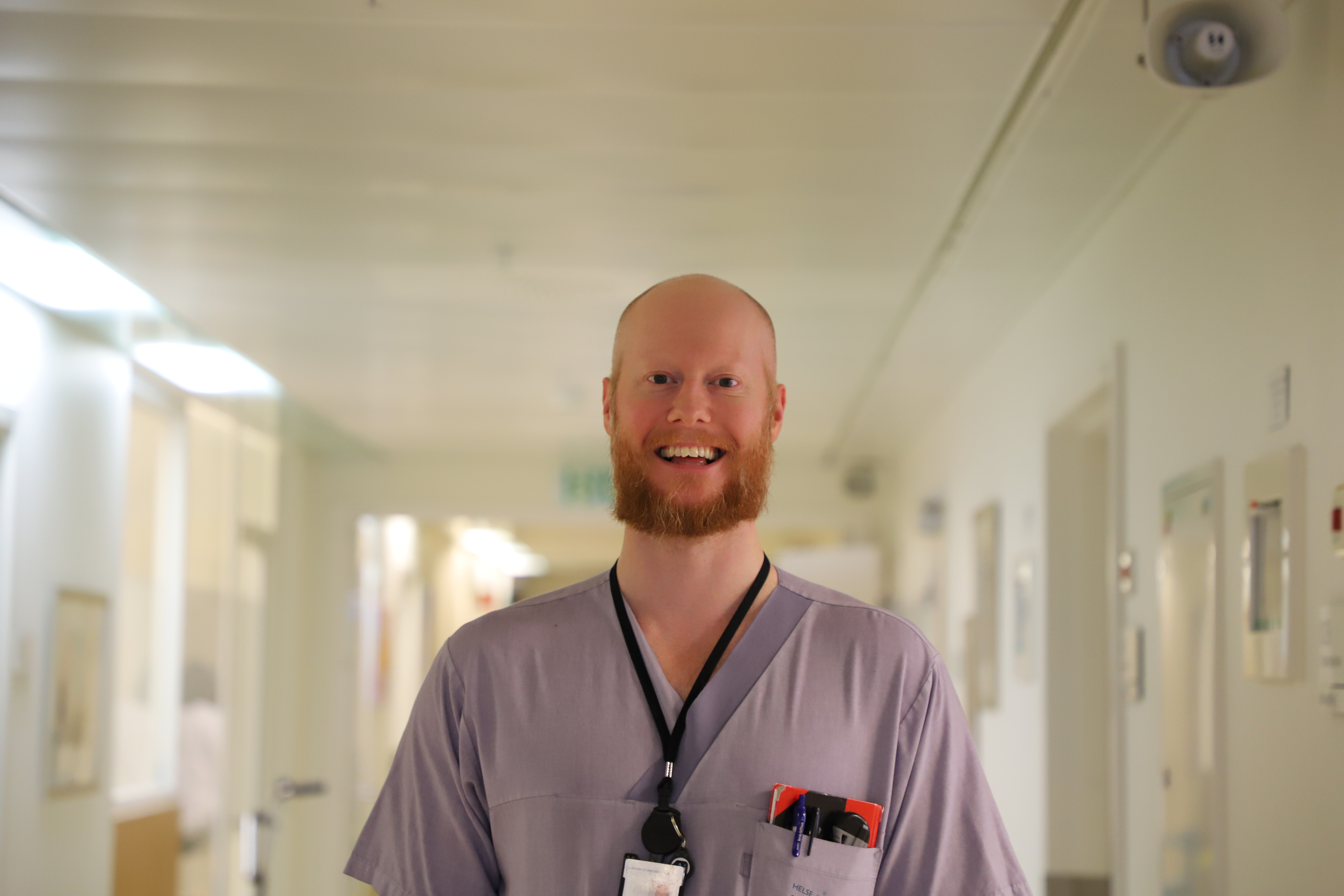 En mann i lyselilla t-skjorte smiler til kamera