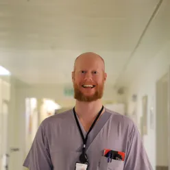 En mann i lyselilla t-skjorte smiler til kamera