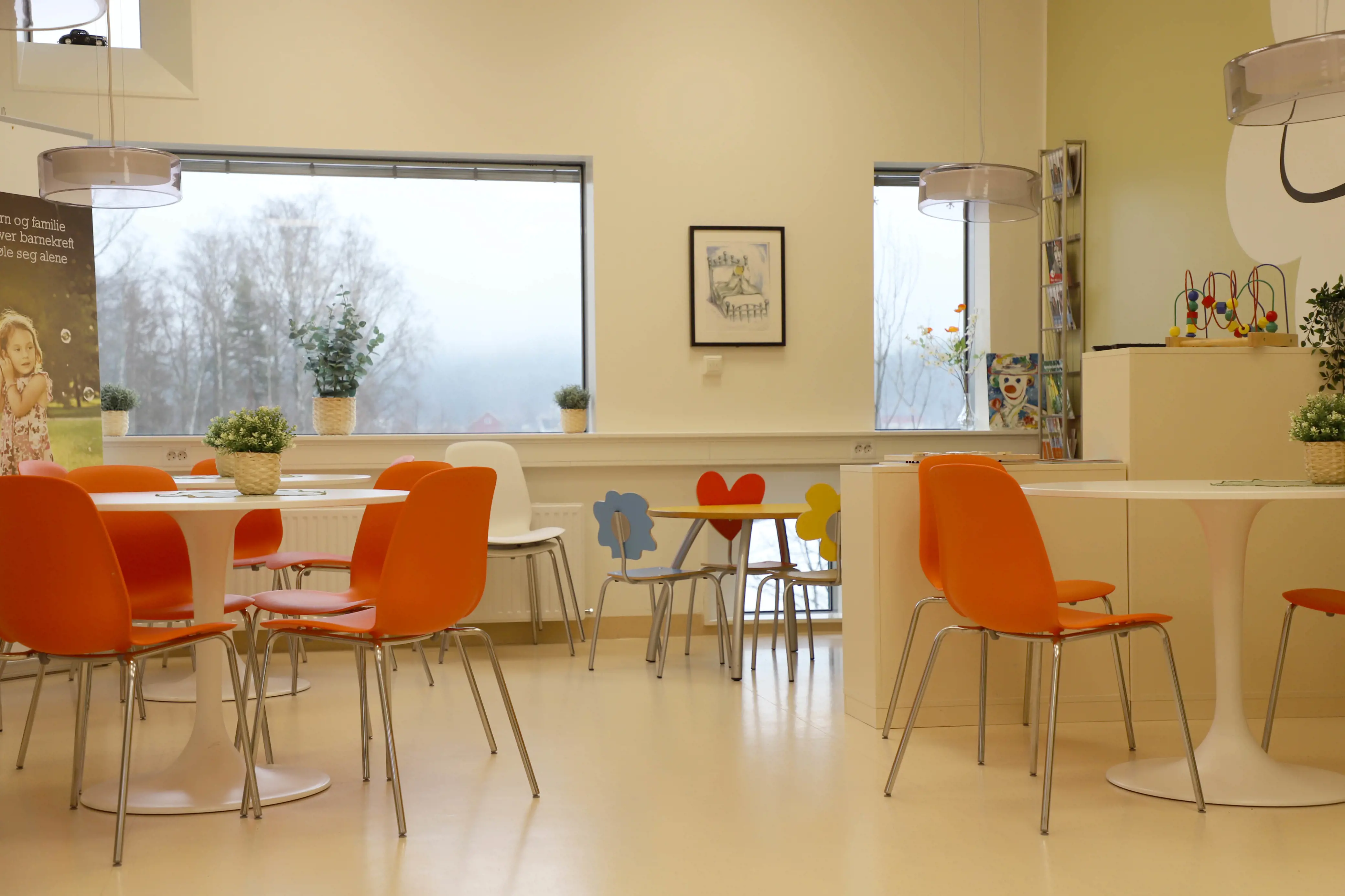En kantine med hvite vegger, hvite bord og oransje stoler.
