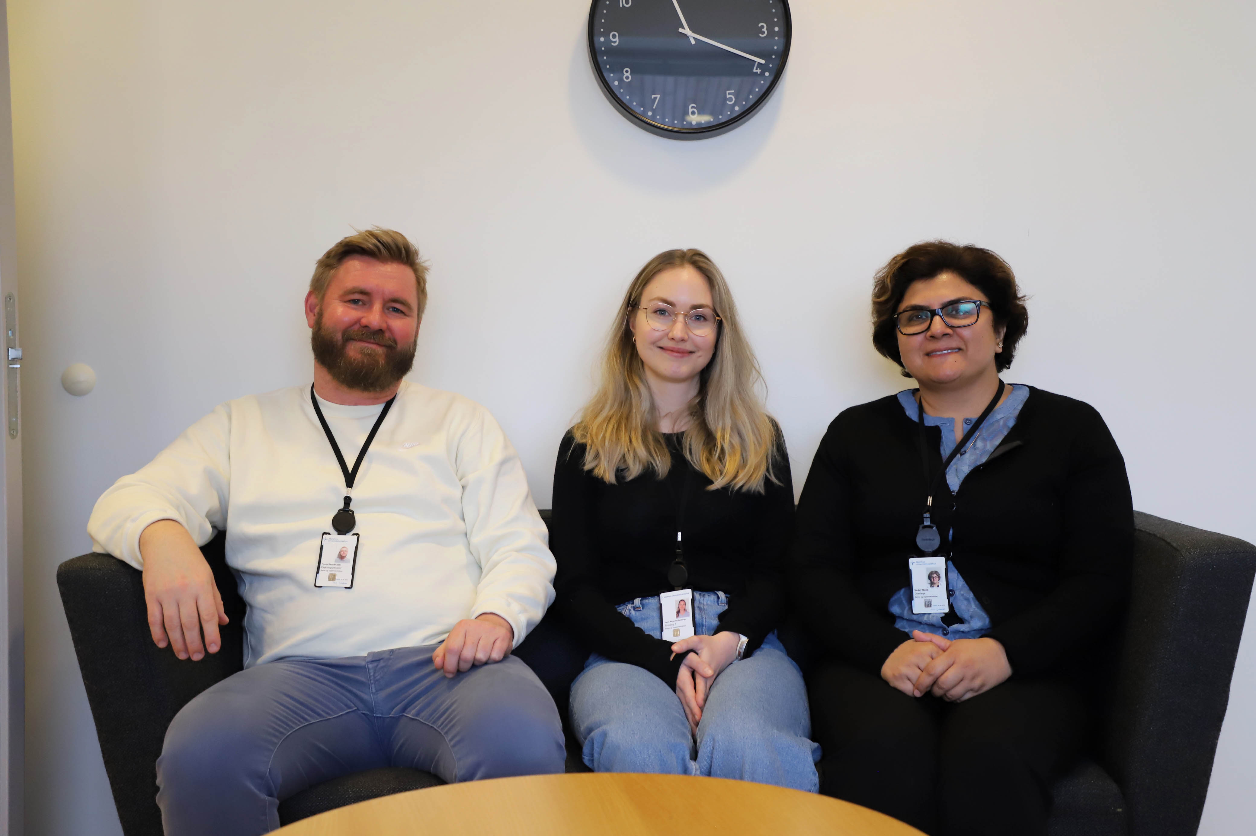 To kvinner og en mann sitter i en sofa og smiler.