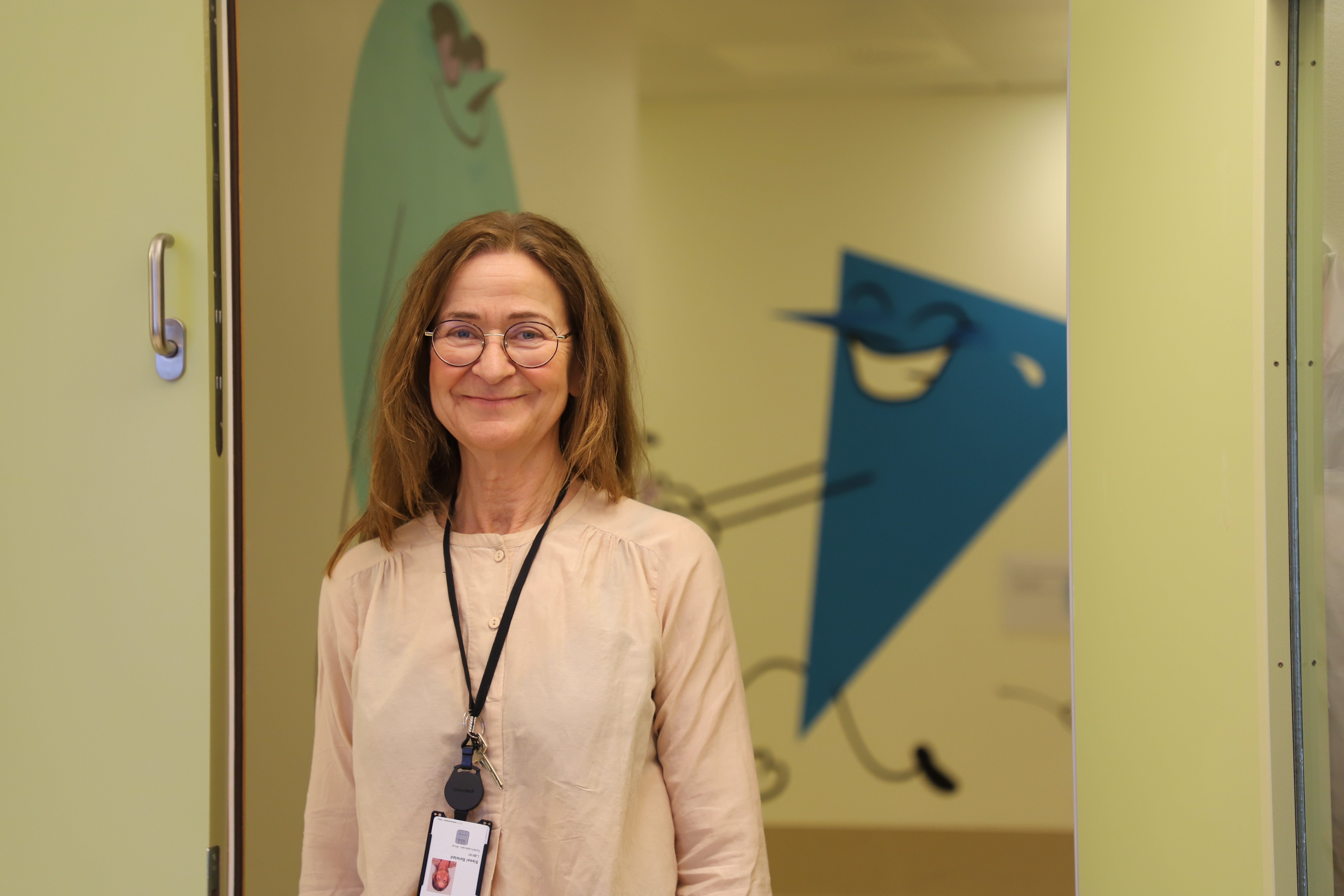 En kvinne med brunt hår og runde briller smiler.