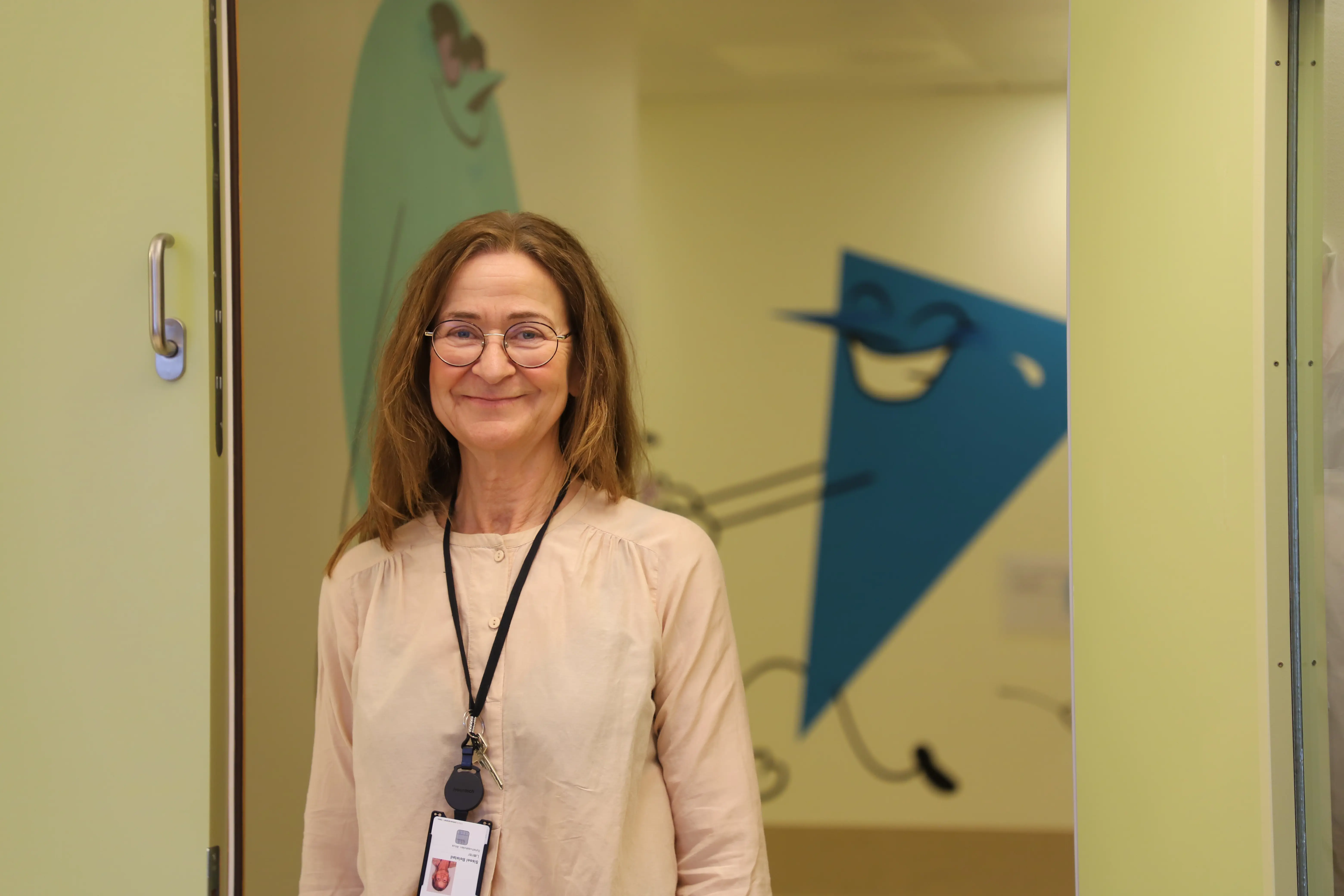 En kvinne med brunt hår og runde briller smiler.