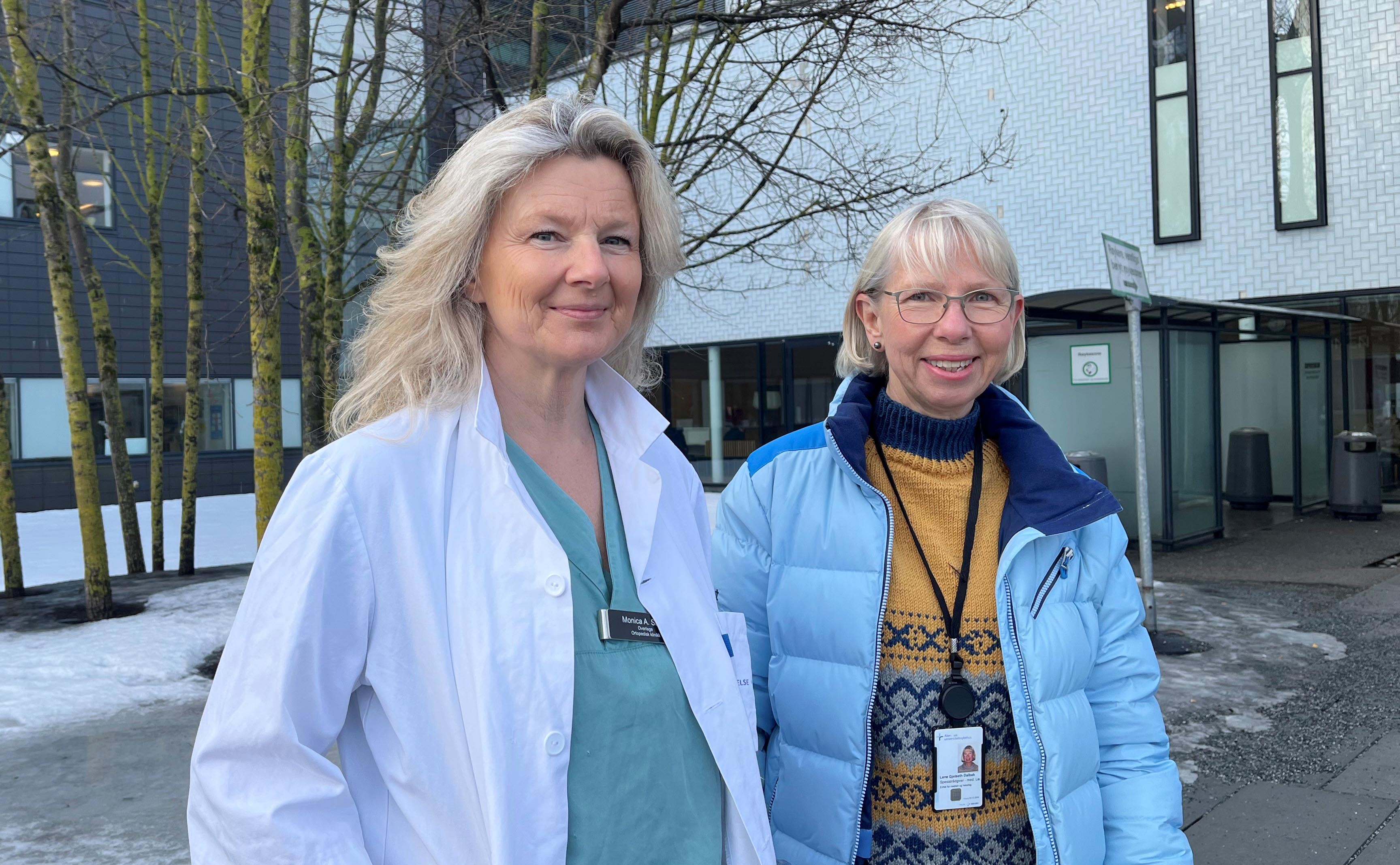 En kvinne i legeuniform og en kvinne med blå jakke smiler 