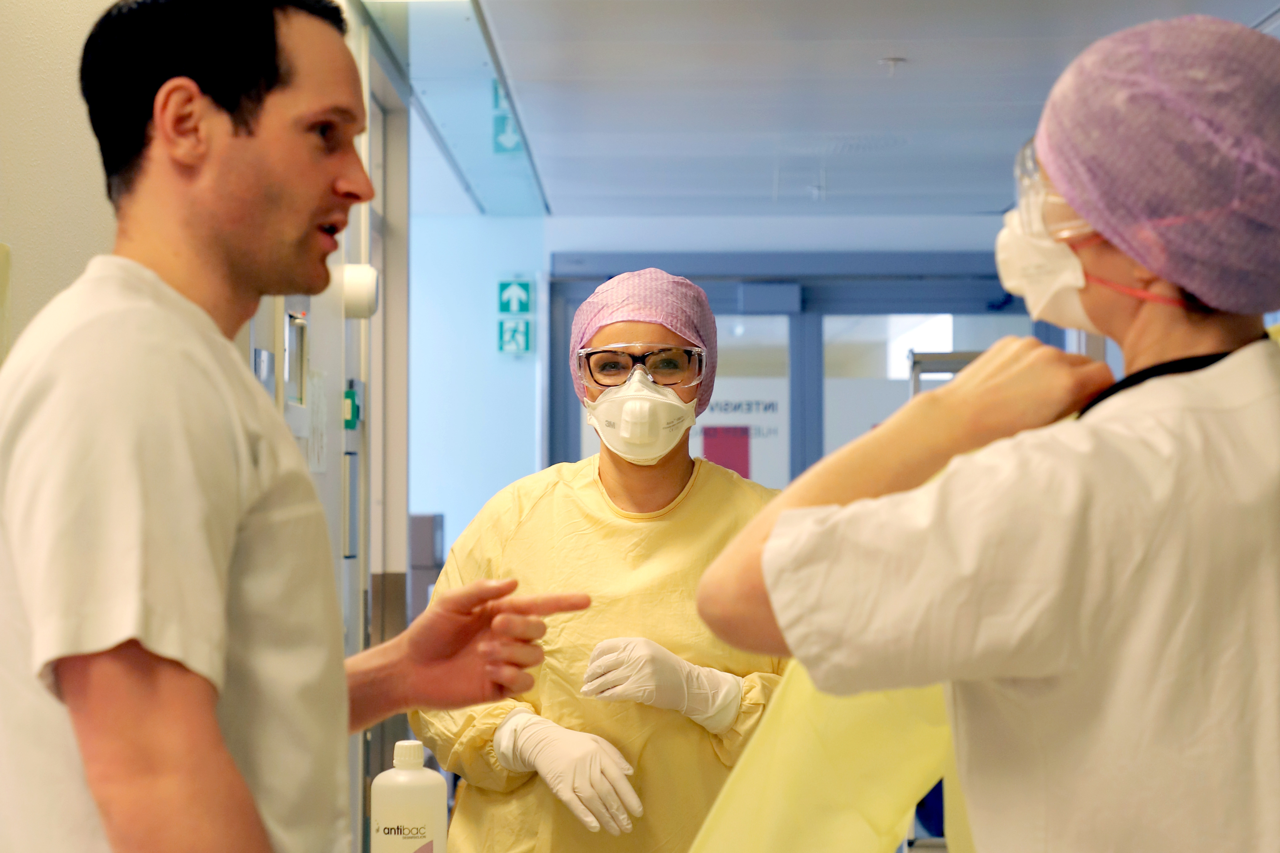 Kvinne i gult smittevernsustyr prater med helsepersonell