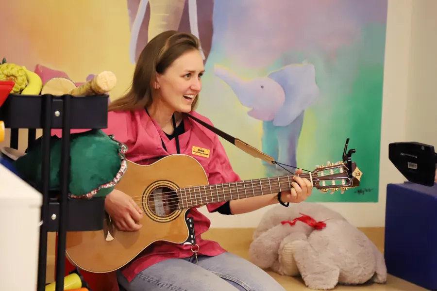 Musikkterapeut spiller gitar i lekerom.