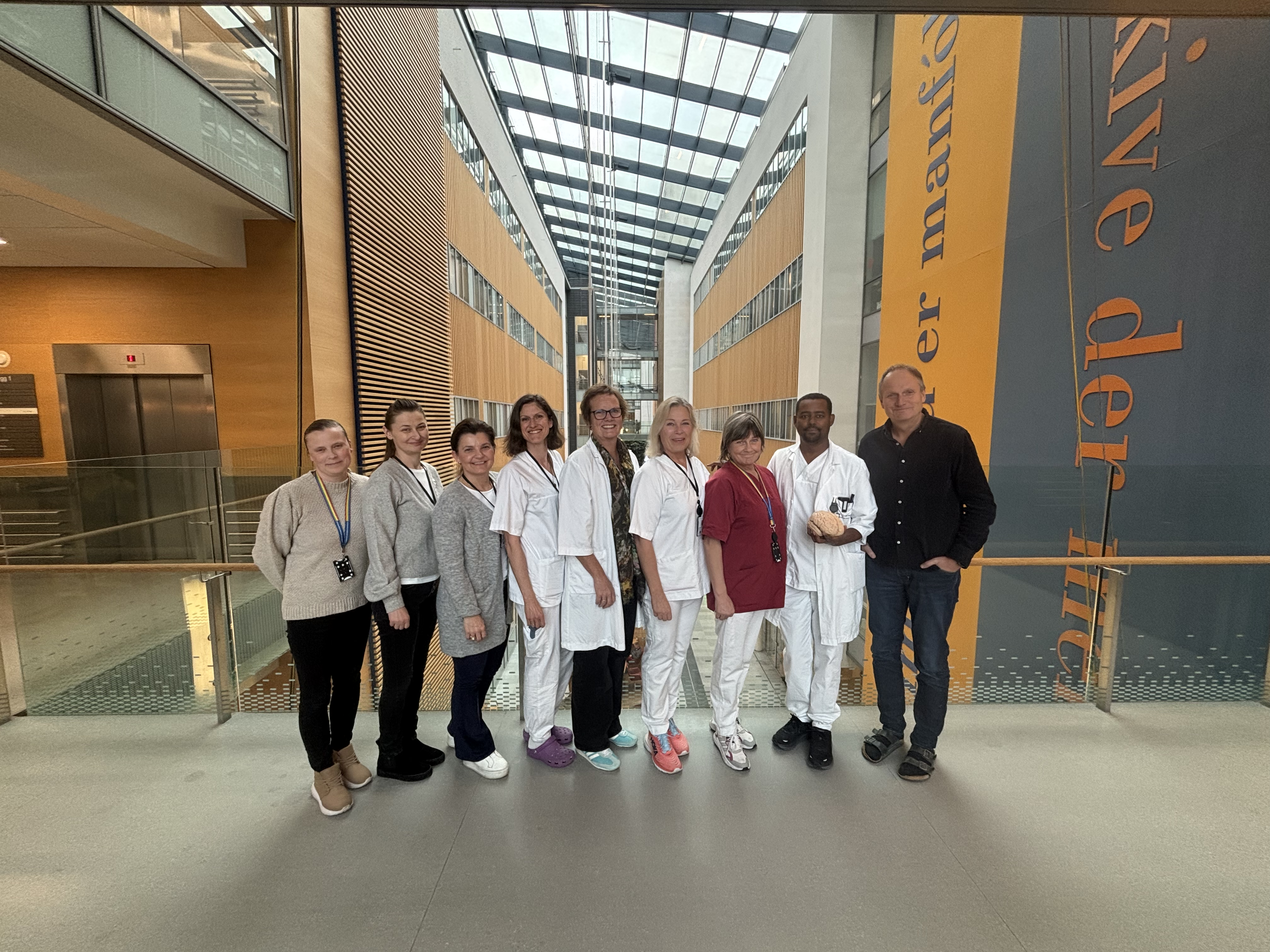 Ansatte fra nevrologisk avdeling står oppstilt inne på sykehuset og smiler mot kamera. Noen har på seg sykehusklær, legefrakker.