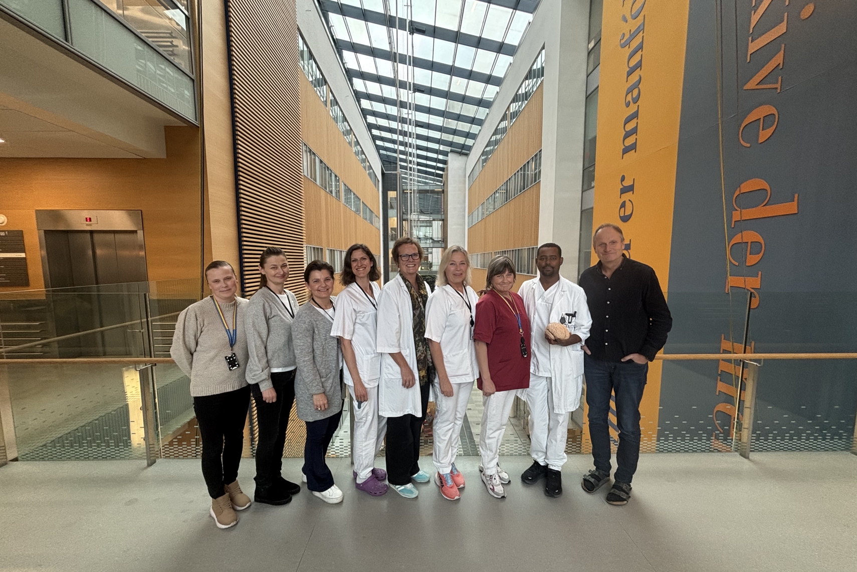 Ansatte fra nevrologisk avdeling står oppstilt inne på sykehuset og smiler mot kamera. Noen har på seg sykehusklær, legefrakker.