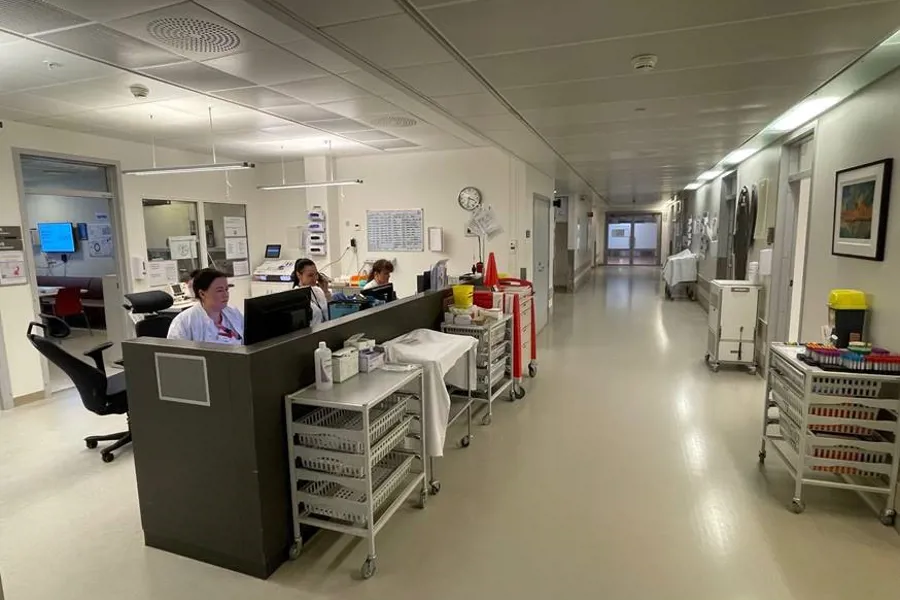 Bilde nedover en sykehusgang ansatte jobber ved arbeidsstasjon på venstre side