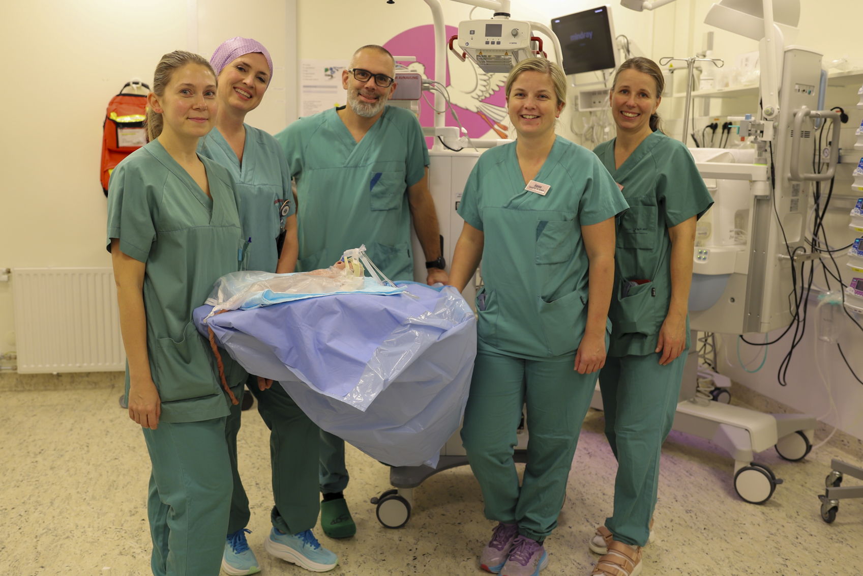 En gruppe mennesker i kirurgisk skrubb som står ved siden av en pasient