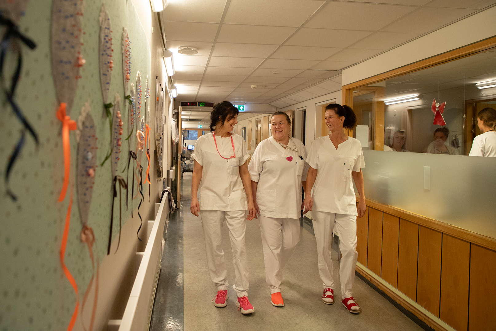 tre helsepersonell kledd i hvitt går nedover sykehuskorridor