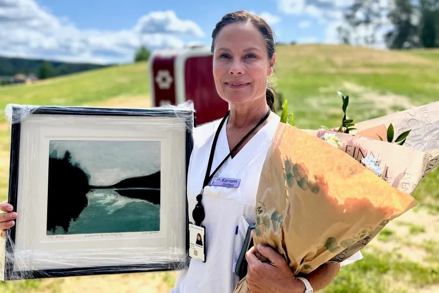 Smilende sykepleier med blomst og bilde utendørs