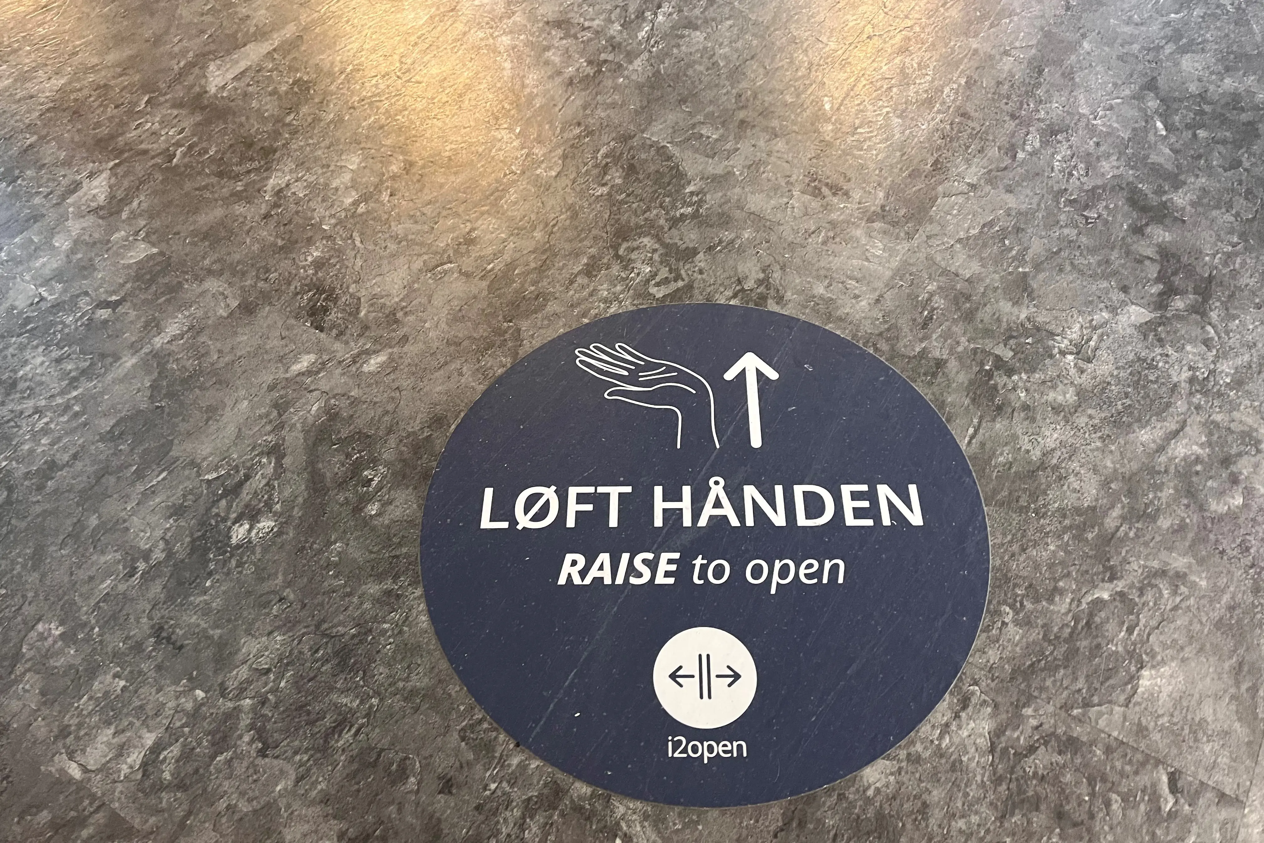 Klistremerke viser hvor det er en berøringsfri døråpner på gulvet. På merket står det