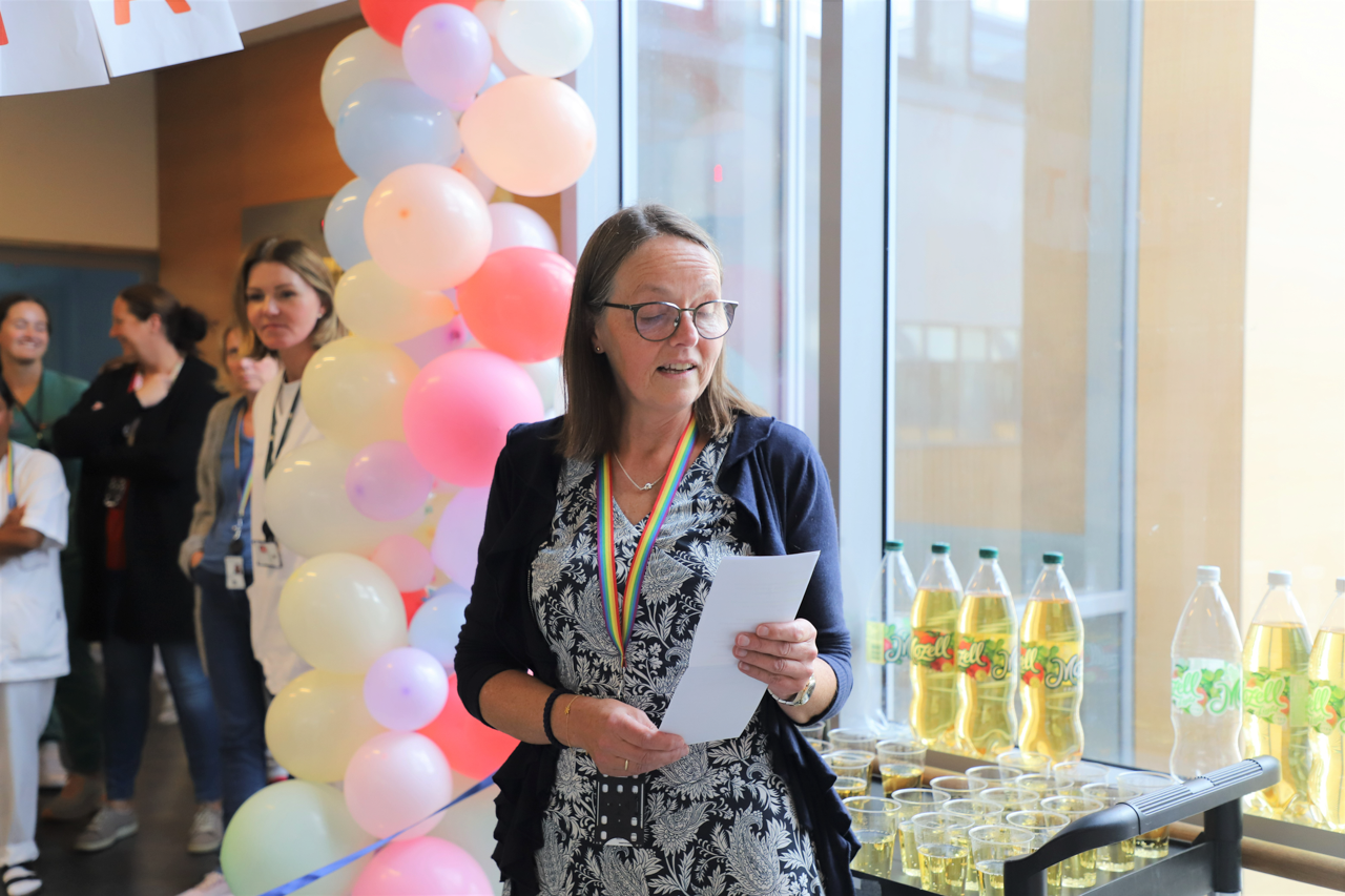 Dame leser opp en tale foran ballonger.
